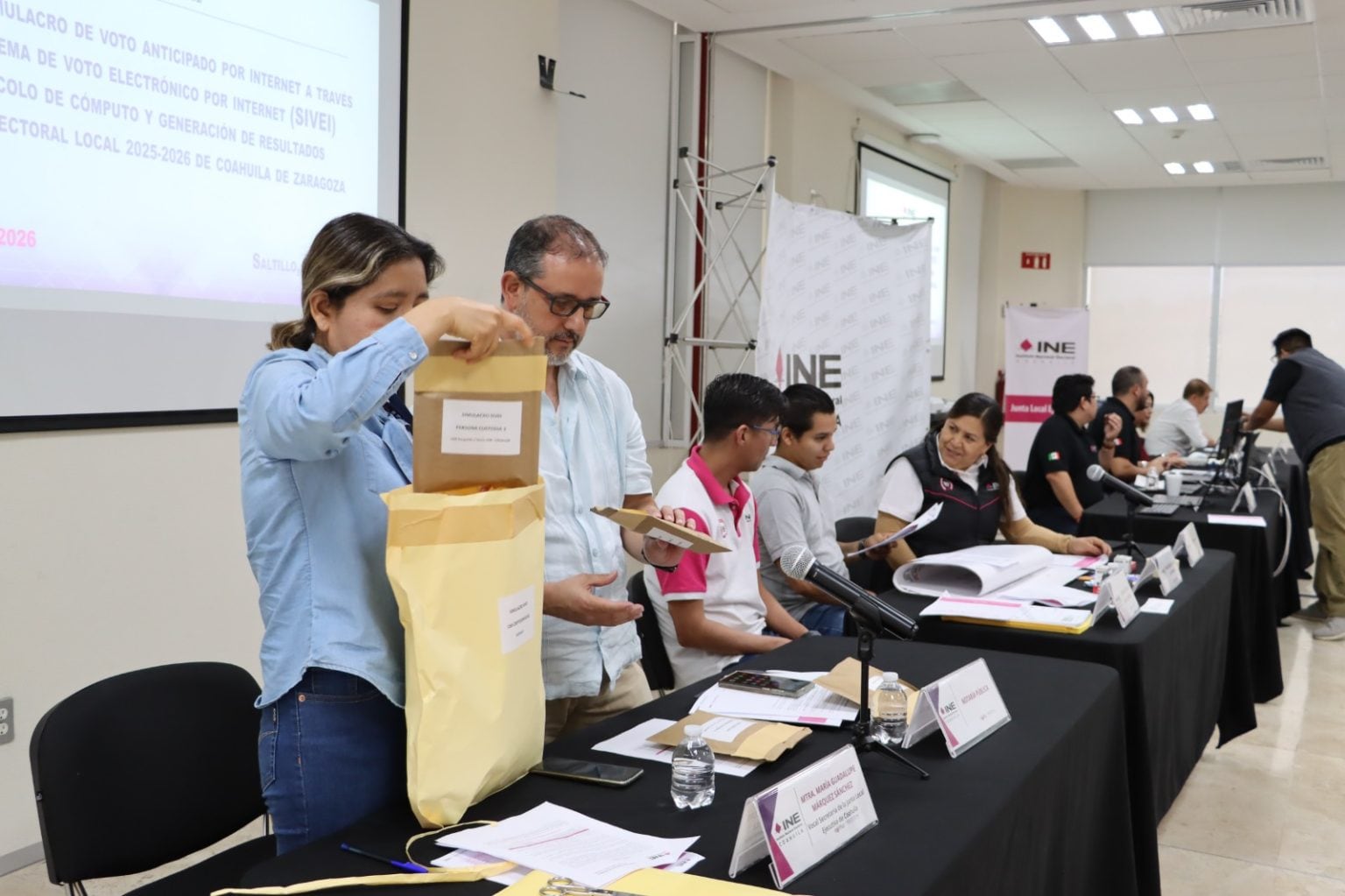 Personal del INE participa en un simulacro de voto electrónico para las elecciones locales 2025-2026 en Coahuila, manejando sobres electorales durante el evento. (INE)