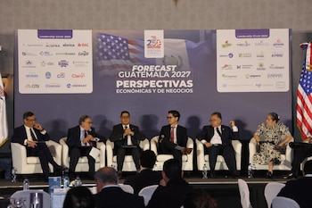 Seis panelistas en un escenario, sentados en sillones blancos; detrás, un cartel con texto 'Forecast Guatemala 2027', logotipos empresariales y banderas de Estados Unidos y Guatemala