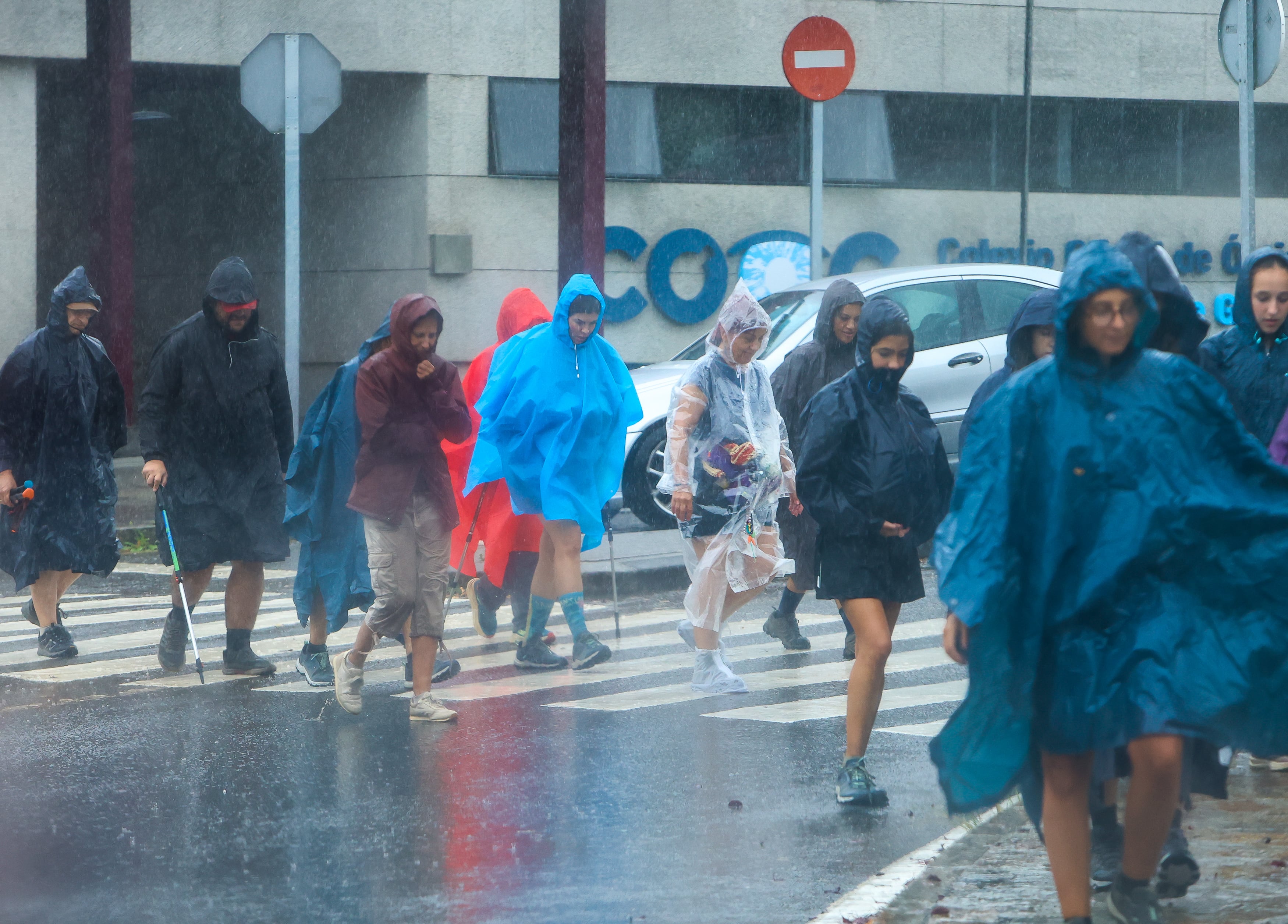 Peregrinos que se encuentran en la última etapa del Camino Francés se protegen este martes de la lluvia. (EFE/Xoán Rey)