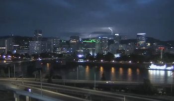 Vista nocturna de un río, un puente con automóviles y edificios altos de una ciudad con relámpagos en el cielo oscuro