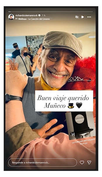 Un hombre de barba gris sonríe, lleva una gorra plana y una bufanda amarilla, y sostiene un objeto rojo con plumas. La imagen incluye un texto y una interfaz de reproductor de música