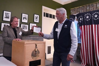 El coordinador de la ciudad, Tom Tillotson, izquierda, recibe la primera boleta de Les Otten, durante la votación de medianoche el día de la elección, el martes 5 de noviembre de 2024, en Dixville Notch, Nueva Hampshire. (AP Foto/Charles Krupa)