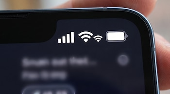 Primer plano de la parte superior de la pantalla de un celular con iconos de señal móvil, WiFi, hotspot, y batería. Un dedo sostiene el dispositivo.