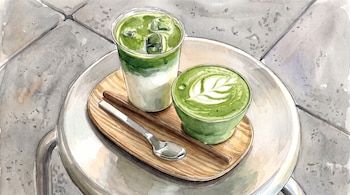 Vaso transparente con té matcha helado y taza verde con té matcha caliente sobre una bandeja de madera con una cuchara.
