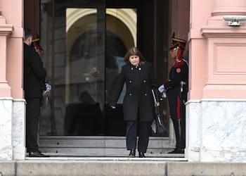 Patricia Bullrich desciende por las escaleras de un edificio de muros rosados custodiado por dos guardias con uniforme tradicional