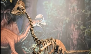 Esqueleto de un dinosaurio con cresta craneal expuesto frente a una pintura de la criatura en un bosque