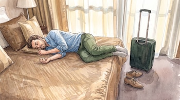 Un hombre duerme de costado en una cama, junto a una maleta verde con asa extendida y unos zapatos en el suelo.