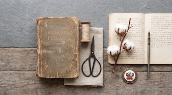 Un libro de Ricardo Palma, un carrete de hilo, tijeras, una rama de algodón, un cuaderno manuscrito, una pluma y una insignia del Perú.
