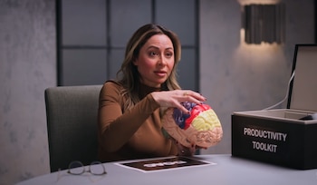 Sahar Yousef sostiene un modelo anatómico de cerebro frente a una mesa con anteojos y una caja rotulada como Productivity Toolkit