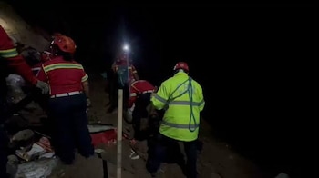 Integrantes de un cuerpo de rescate con cascos, linternas y chaquetas reflectantes trabajan de noche en un terreno oscuro con escombros