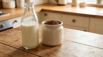 Una botella de vidrio con leche y un recipiente de cerámica con gránulos de café instantáneo sobre una mesa de madera. Cocina en segundo plano.
