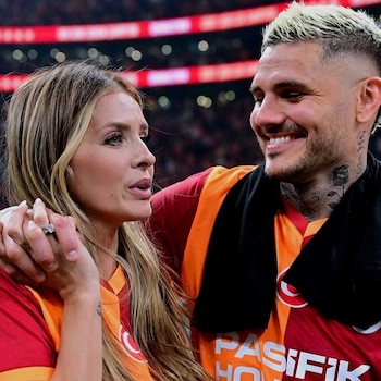 Mauro Icardi sonríe mientras China Suárez lo mira, tomados de la mano, ambos con camisetas del Galatasaray en un estadio iluminado