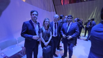 Cuatro personas con vestimenta formal posan de pie en un evento iluminado con luces azules