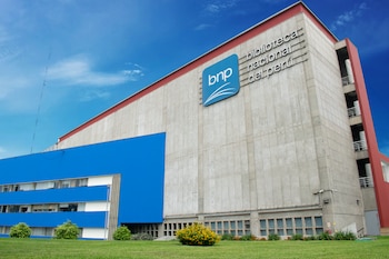 Fachada del edificio de la Biblioteca Nacional del Perú con logotipo azul, muros de concreto, áreas verdes y cielo despejado
