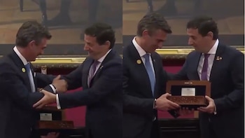 Dos hombres con traje intercambian un apretón de manos y un objeto dentro de una caja de madera en un salón