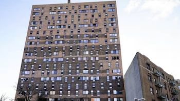 Vista exterior de un alto edificio de apartamentos de ladrillo con muchas ventanas rotas y huecos oscuros. A la derecha, parte de un edificio de ladrillo más bajo