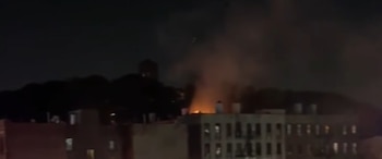 Vista nocturna de un incendio en el tejado de un edificio con llamas brillantes y una columna de humo ascendente. Otros edificios oscuros son visibles detrás