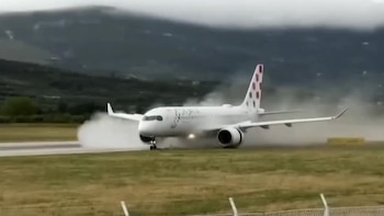 Avión blanco de Croatia Airlines con cola roja y blanca aterrizando en pista, con vapor o rocío alrededor de las ruedas, y montañas verdes al fondo