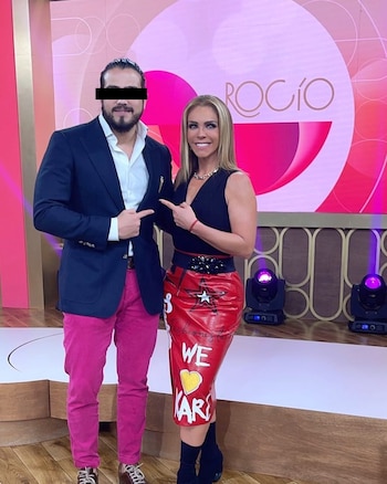 Rocío Sánchez Azuara, con blusa negra y falda roja, y Andrés Tovar, con blazer azul y pantalones fucsia, se señalan mutuamente en un set de televisión
