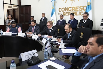 Funcionarios del Congreso de Guatemala en una sala de reuniones, sentados alrededor de una mesa, con documentos, micrófonos y banderas de Guatemala