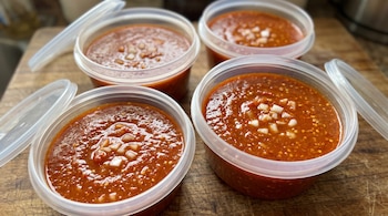 Cuatro recipientes transparentes de plástico llenos de salsa roja con cebolla picada en la superficie sobre una tabla de madera.