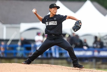 Una jugadora de béisbol con uniforme negro, que dice Los Angeles, lanza una bola desde un montículo de tierra, con guante y zapatillas con tacos