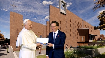 El Papa, vestido de blanco, entrega una caja con una llave dorada al alcalde Almeida, vestido de traje oscuro, frente a una iglesia de ladrillo con una cruz y campanas.