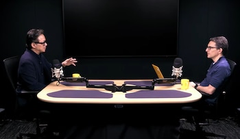 Dr. William Li, con gafas y chaqueta oscura, gesticula mientras habla con otro hombre en un estudio. Ambos están sentados en una mesa con micrófonos y tazas amarillas