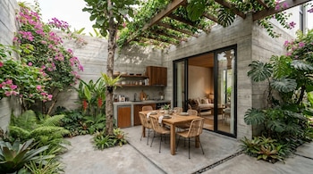 Pátio externo com paredes de concreto, plantas verdes e flores rosa, cozinha, mesa de jantar com seis cadeiras e portas de vidro para a sala.