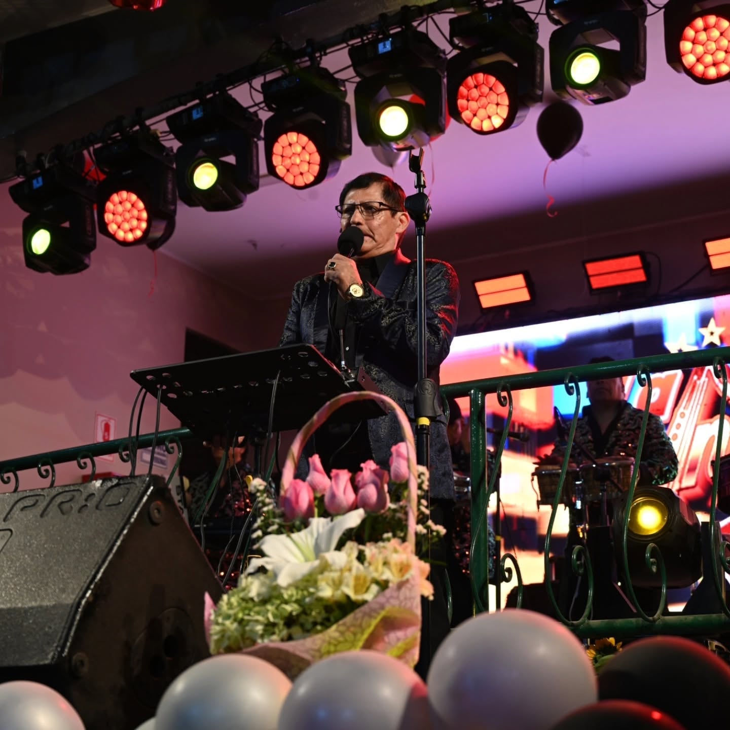 El cantante peruano Pascualillo Coronado interpreta un tema musical durante una presentación en vivo sobre un escenario iluminado.