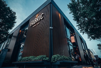 Edificio de esquina con letrero luminoso de Fabric Sushi Bar, fachada de listones verticales, ventanales de vidrio y plantas en la base