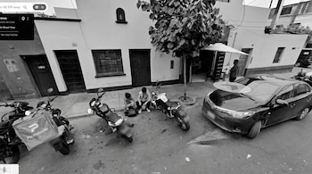 Fotografía en blanco y negro de dos personas sentadas en la acera entre motocicletas y un automóvil estacionado frente a un inmueble.