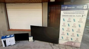 Dos televisores, la caja de una consola de videojuegos y un cartel de la Policía de la Provincia de Buenos Aires frente a una puerta