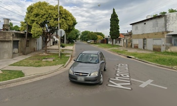 Imagen de una calle residencial en Rosario con un coche gris en primer plano, flanqueada por casas y árboles bajo un cielo nublado