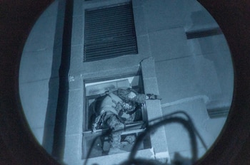 Hombre con uniforme militar y equipamiento táctico sube por la ventana de un edificio, con efecto de visión nocturna y borde circular negro