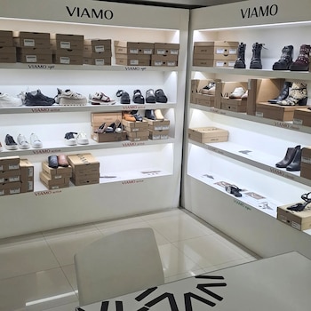 Interior de tienda de calzado Viamo con estantes blancos que exhiben una variedad de zapatos y numerosas cajas, incluyendo zapatillas, botas y sandalias