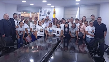Un grupo de personas posa en una oficina. La mayoría son mujeres con camisetas blancas estampadas, junto a hombres y una mesa de conferencia oscura