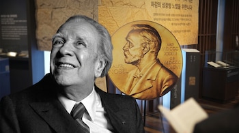 Retrato en blanco y negro de Jorge Luis Borges sobrepuesto ante una medalla dorada del Premio Nobel y una sala con vitrinas.
