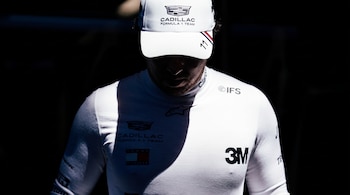 Un piloto con gorra y prenda blanca que exhiben el logotipo de Cadillac Formula 1 Team, el número once y otras marcas.