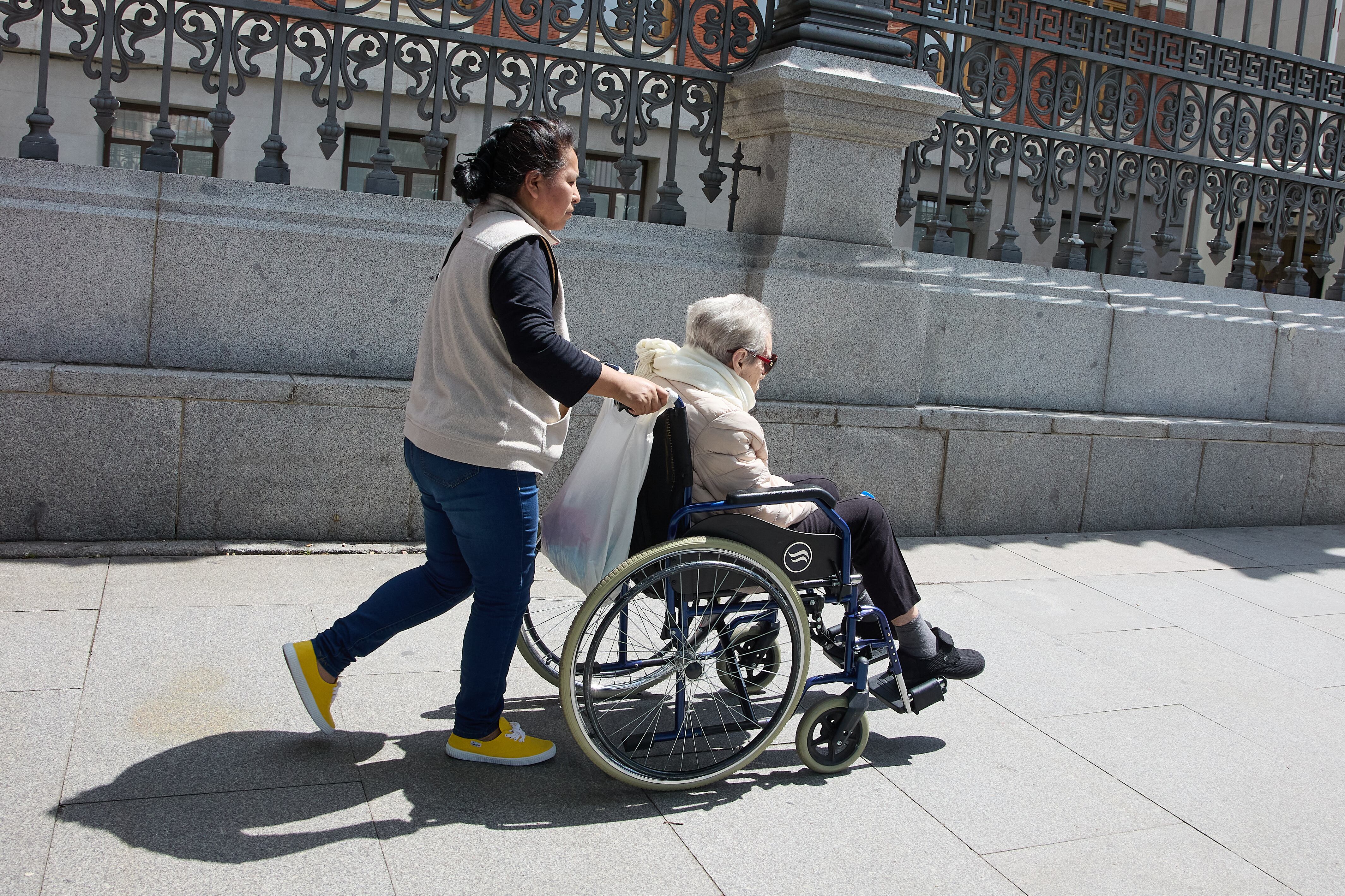 Una mujer mayor en silla de ruedas y su cuidadora pasean por el centro de la ciudad, a 4 de junio de 2023, en Madrid (España). (Jesús Hellín - Europa Press)