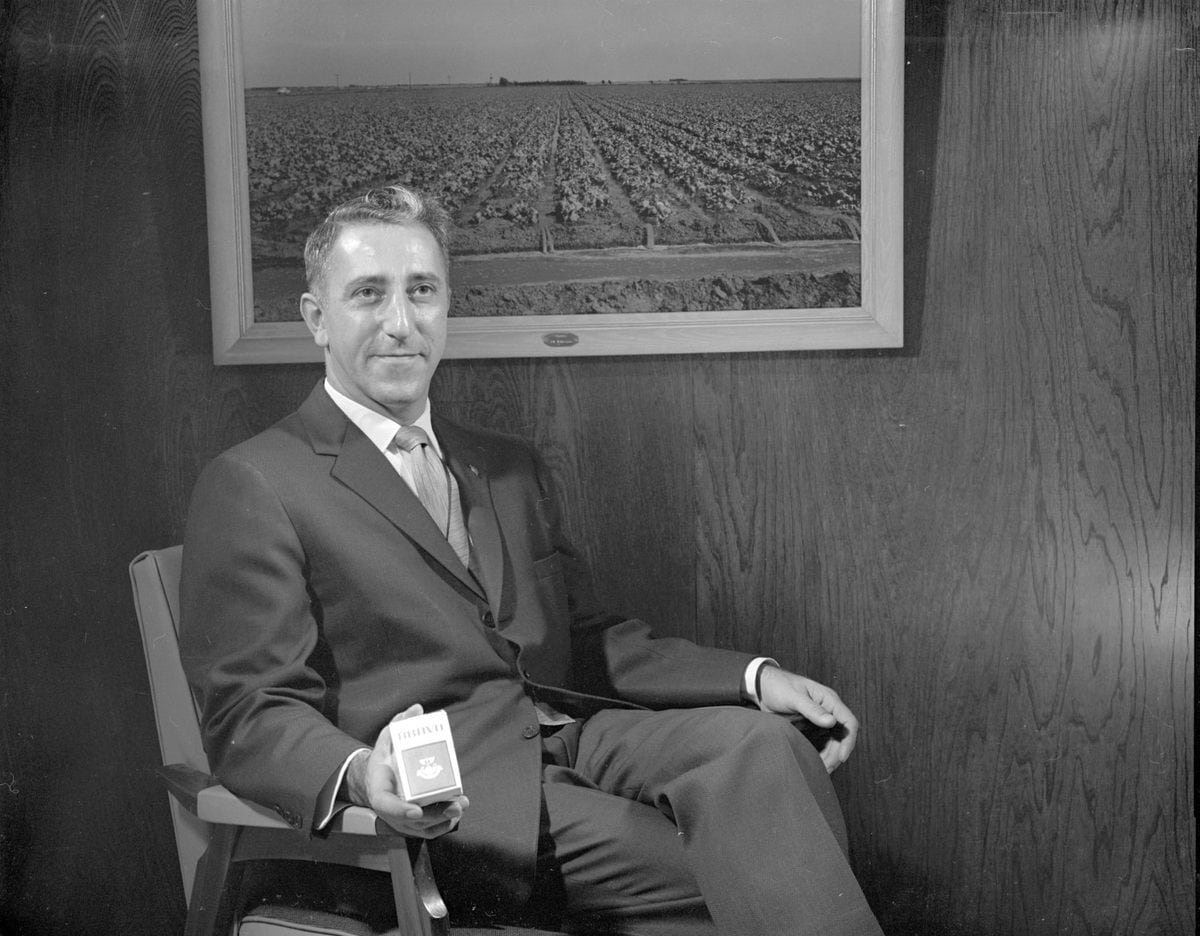 En esta foto de la década de 1960, Puzant Torigion sostiene con orgullo una caja de Bravo Smokes. La fotografía del fondo muestra un campo de lechugas. Bill Bradly / Cortesía de la Biblioteca del Condado de Deaf Smith
