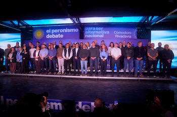 Un grupo de personas sobre un escenario frente a carteles con leyendas políticas y banderas argentinas en un salón iluminado
