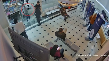 Imagen de cámara de seguridad que muestra a una mujer con sudadera de estampado animal en un mostrador de una oficina, mientras otras personas esperan sentadas