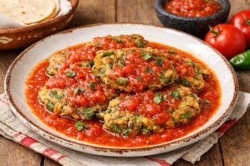Um prato de panquecas de feijão verde com molho de tomate e salsa picada, com tortilhas numa cesta, tomate, pimenta e uma tigela de molho.