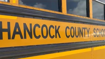 Vista lateral de un autobús escolar amarillo con franjas negras, mostrando la inscripción 'HANCOCK COUNTY SCHOOL' en letras oscuras bajo las ventanas