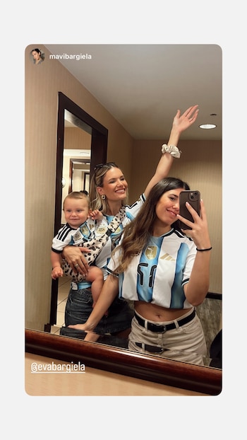 Una mujer se toma una selfie en un espejo con otra mujer que sostiene a un bebé, los tres visten camisetas celestes y blancas de Argentina