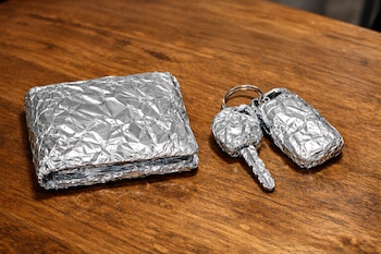 Una billetera y unas llaves de auto, incluyendo un mando a distancia, se encuentran cubiertas con papel aluminio sobre una mesa de madera.