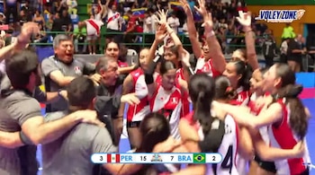 Un grupo de jugadoras de voleibol con uniforme rojo y blanco abraza al cuerpo técnico en la cancha