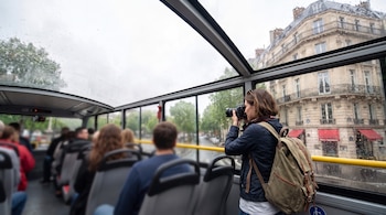 Pasajeros en el interior de un autobús con techo de cristal y una mujer tomando una fotografía junto a la ventana.