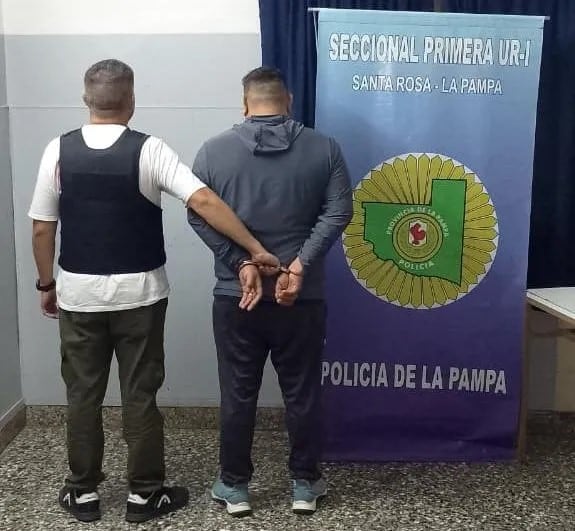 Un agente de policía escoltando al sospechoso de haber apuntado y gatillado a un hombre y su hijo en La Pampa